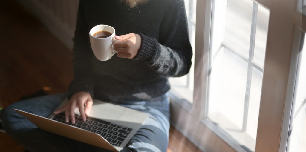 woman-using-laptop-while-holding-a-cup-of-coffee-3759083